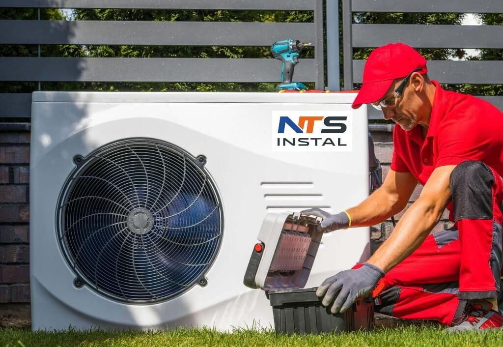 serwis high » Centrum Instalacji grzewczych | Rekuperacji | Klimatyzacji | NTS-Instal » Centrum Instalacji grzewczych | Rekuperacji | Klimatyzacji | NTS-Instal HVAC technician in red uniform servicing an outdoor air conditioner condenser unit with tools nearby on the ground behind him
